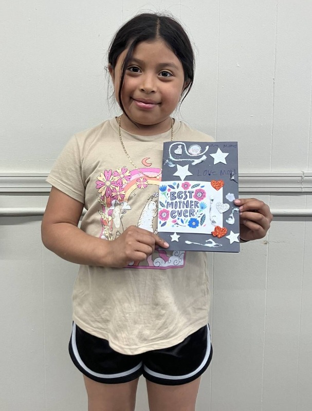 A young girl holding a card she made for Mother's Day at a Bayshore community event