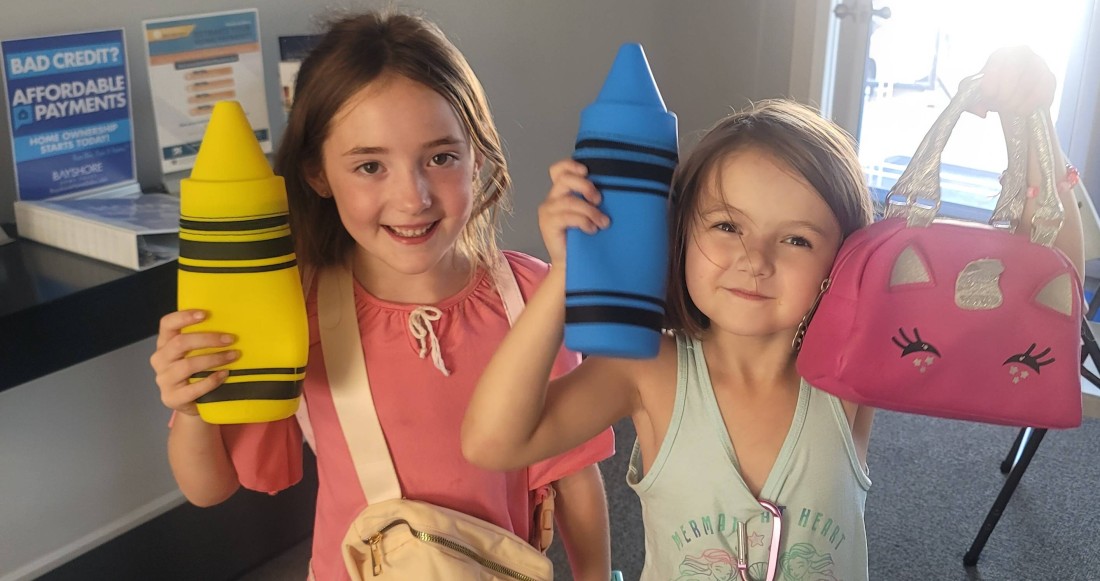 Two girls hold crayon-shaped toys at a Bayshore back to school bash community event