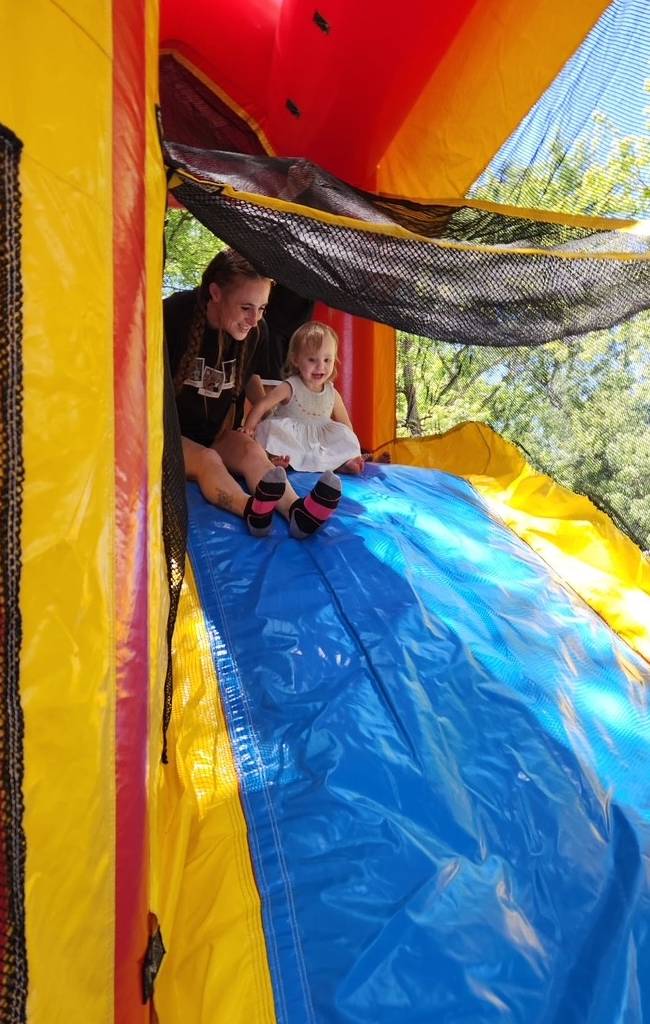 A toddler and her mom sit at the top of an inflatable slide at a Bayshore community event