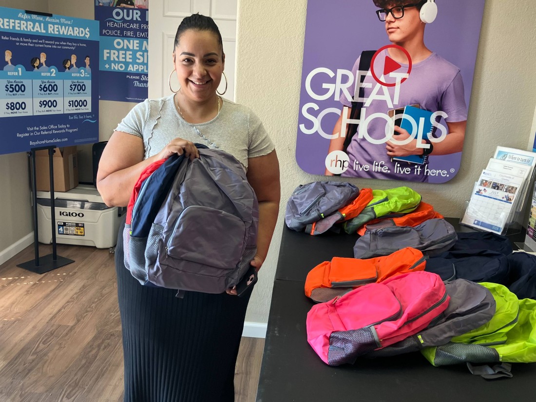 A Bayshore resident holds up a backpack next to a table of giveaway backpacks