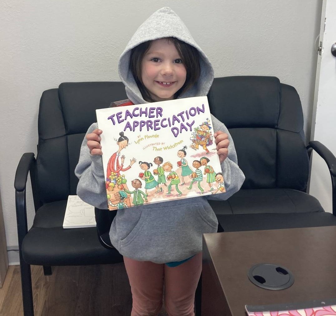 A girl holds up a Teacher Appreciation Day book as part of a kids' event at a Bayshore manufactured home community