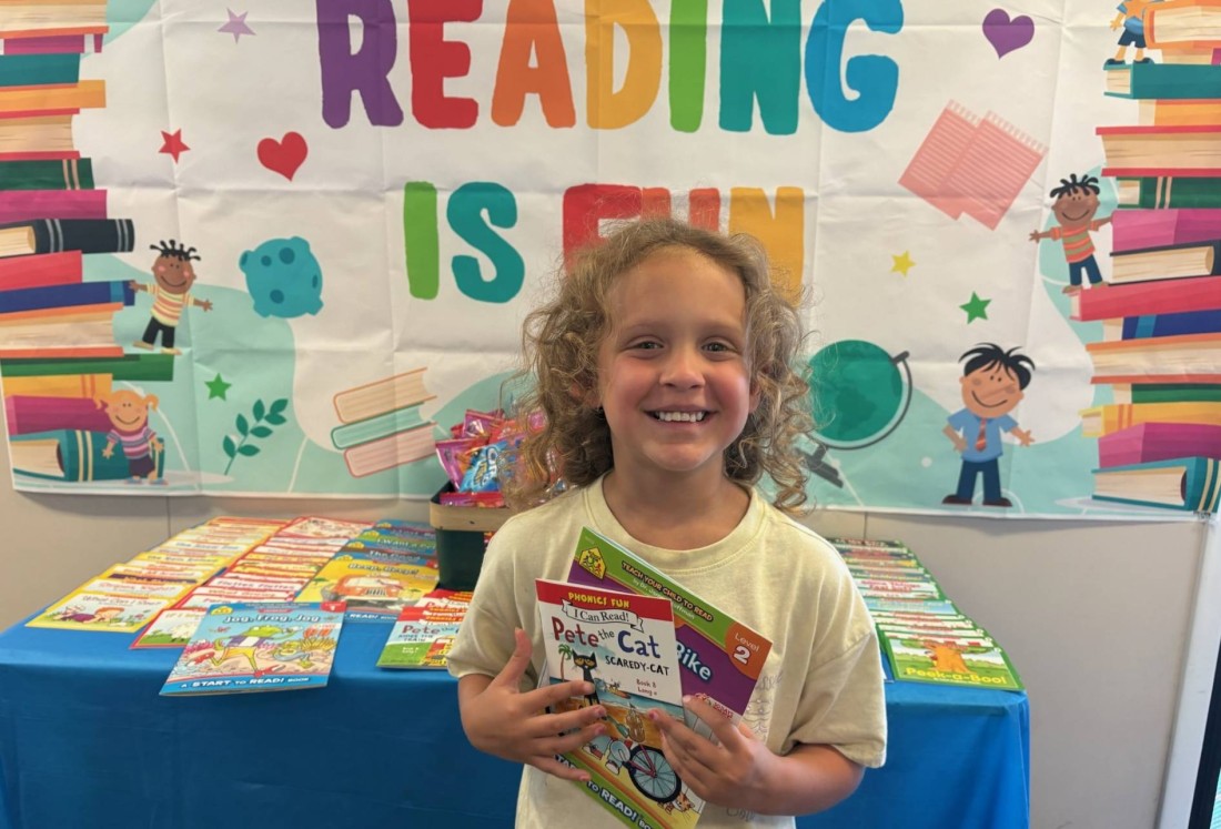 A child poses with their favorite books at a book fair in their manufactured home community