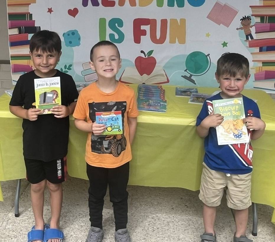 Three young boys pose with book fair books at their manufactured home community's reading event