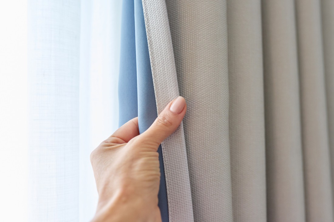 Closeup of a woman’s hand drawing a set of bright summery blackout curtains closed