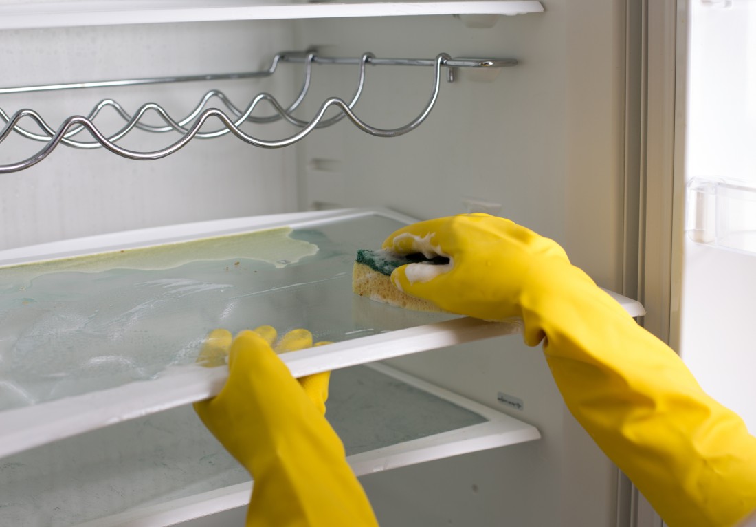 Person wearing gloves and deep cleaning the inside of a refrigerator